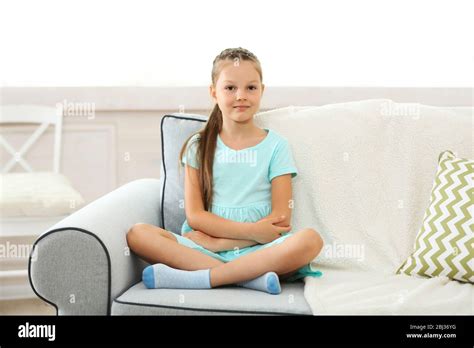 Beautiful little girl sitting on sofa, on home interior background ...