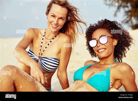 Two smiling young female friends wearing bikinis suntanning together on ... 