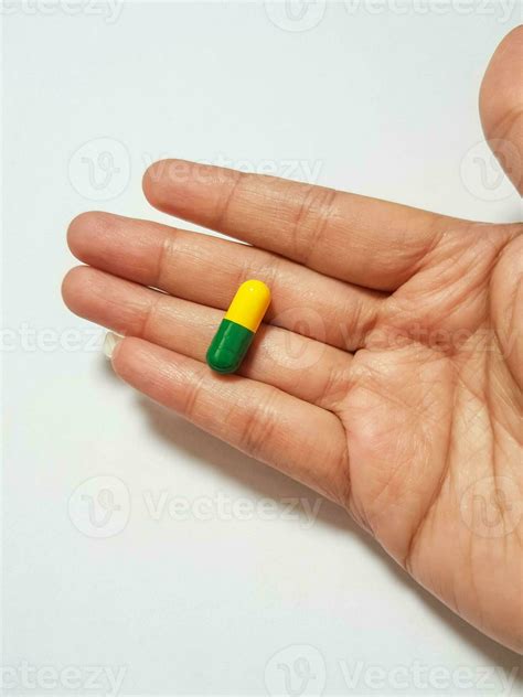 Isolated white photo of a green and yellow capsule sitting on a palm ...