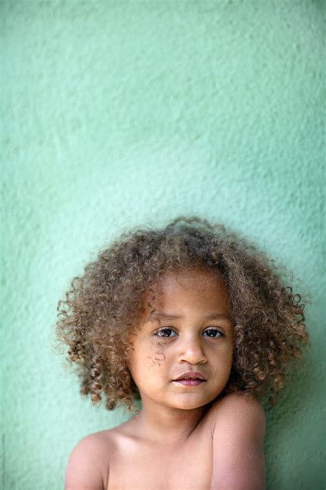 "Beautiful Mixed Race Child Standing Up Against A Green Wall" by