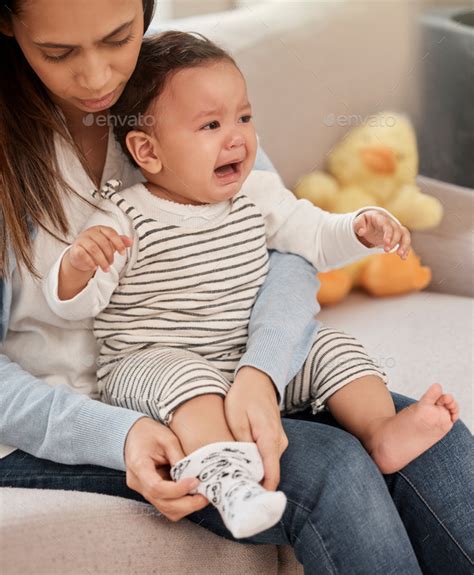 Shot of a young baby girl crying while her mother changes her clothes ...