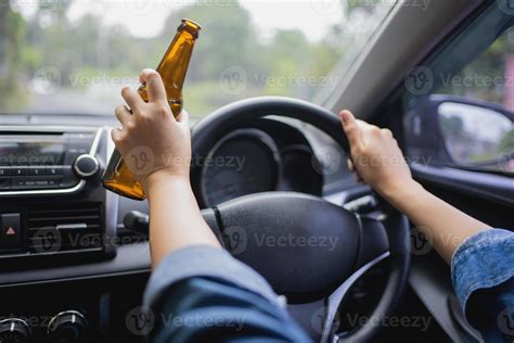 Woman is drinking a bottle of beer while driving a car. Breaking the
