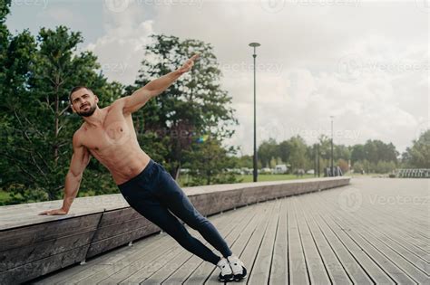 Handsome serious man stands in side plank, has perfect body