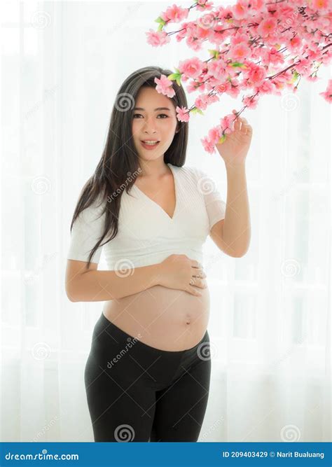 Pregnant Beautiful Woman Stand To Hold Your Stomach and Flowers in a